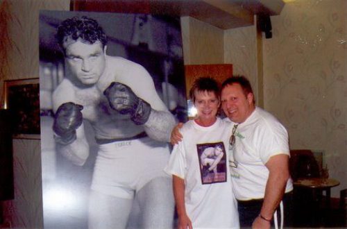 A man and woman posing in front of a large photo of a boxer.