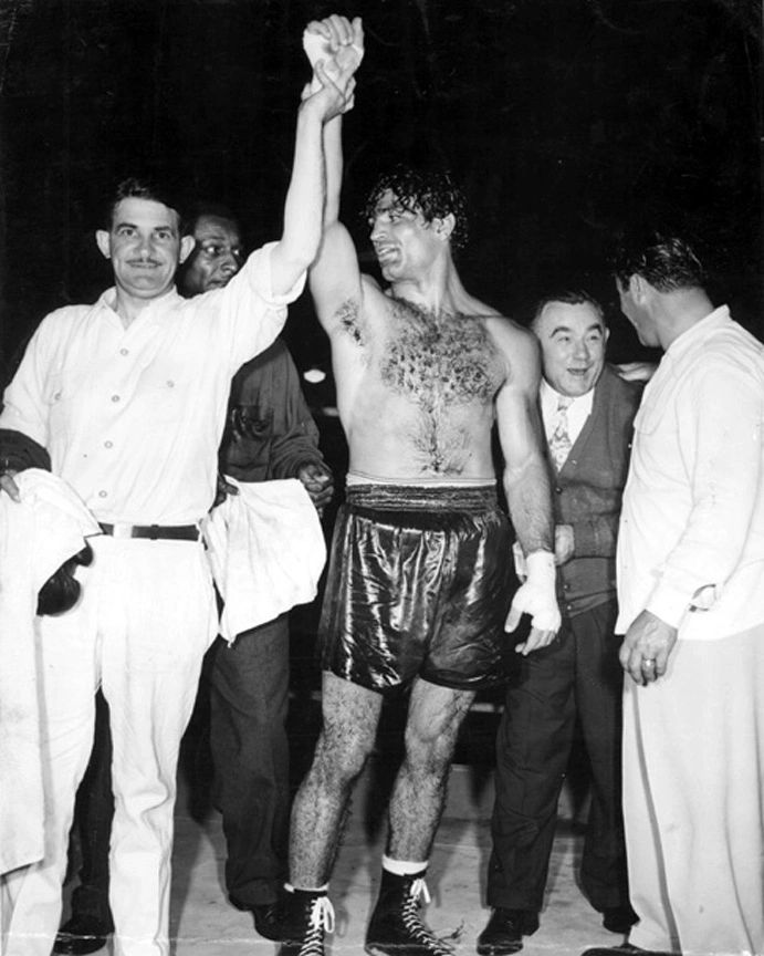 A man in boxing shorts raises his hand.