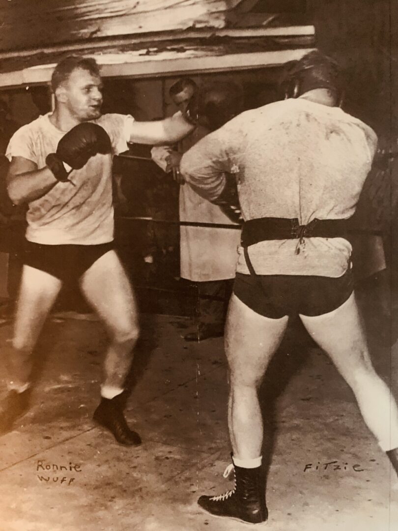 Two men in shorts and trunks are boxing.